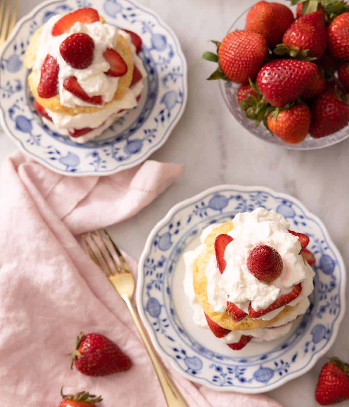 Overhead view of 2 strawberry shortcakes and a bowl of strawberries.
