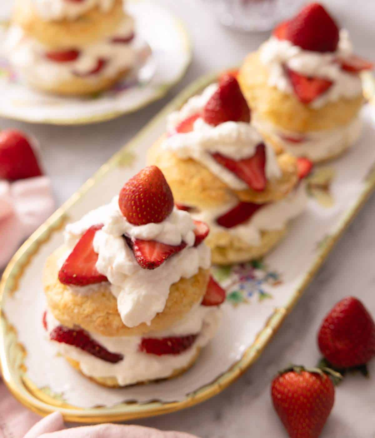 A narrow platter of 3 strawberry shortcakes, only one in focus.