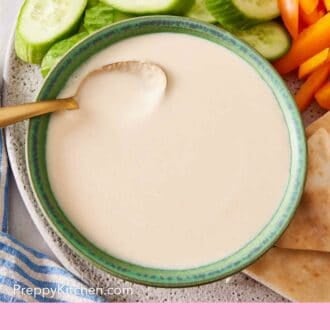 Pinterest graphic showing an overhead shot of tahini sauce on a platter with cut veggies.