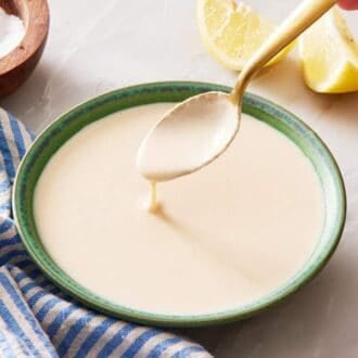 Tahini sauce with a spoon dipped into it. A striped linen and lemon wedges on the side.