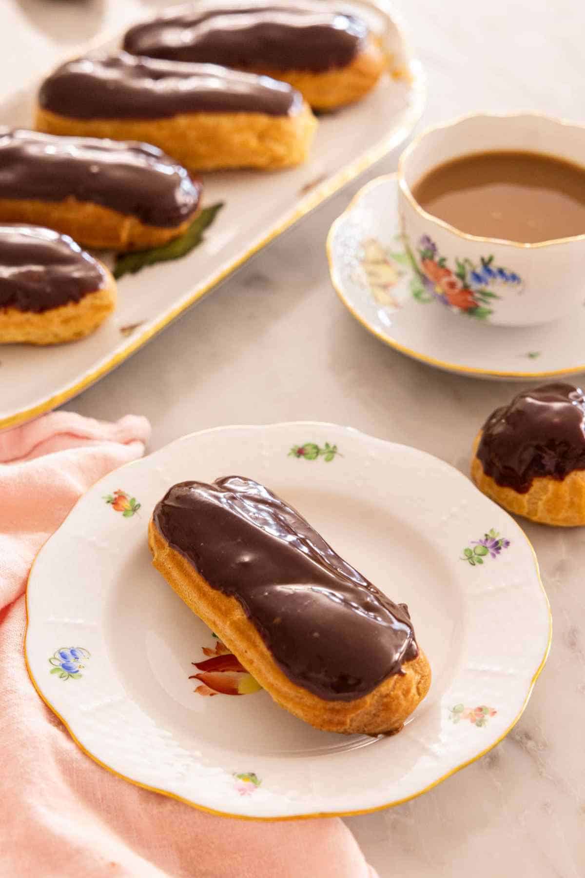 An eclair on a plate with more eclairs on a platter behind it.