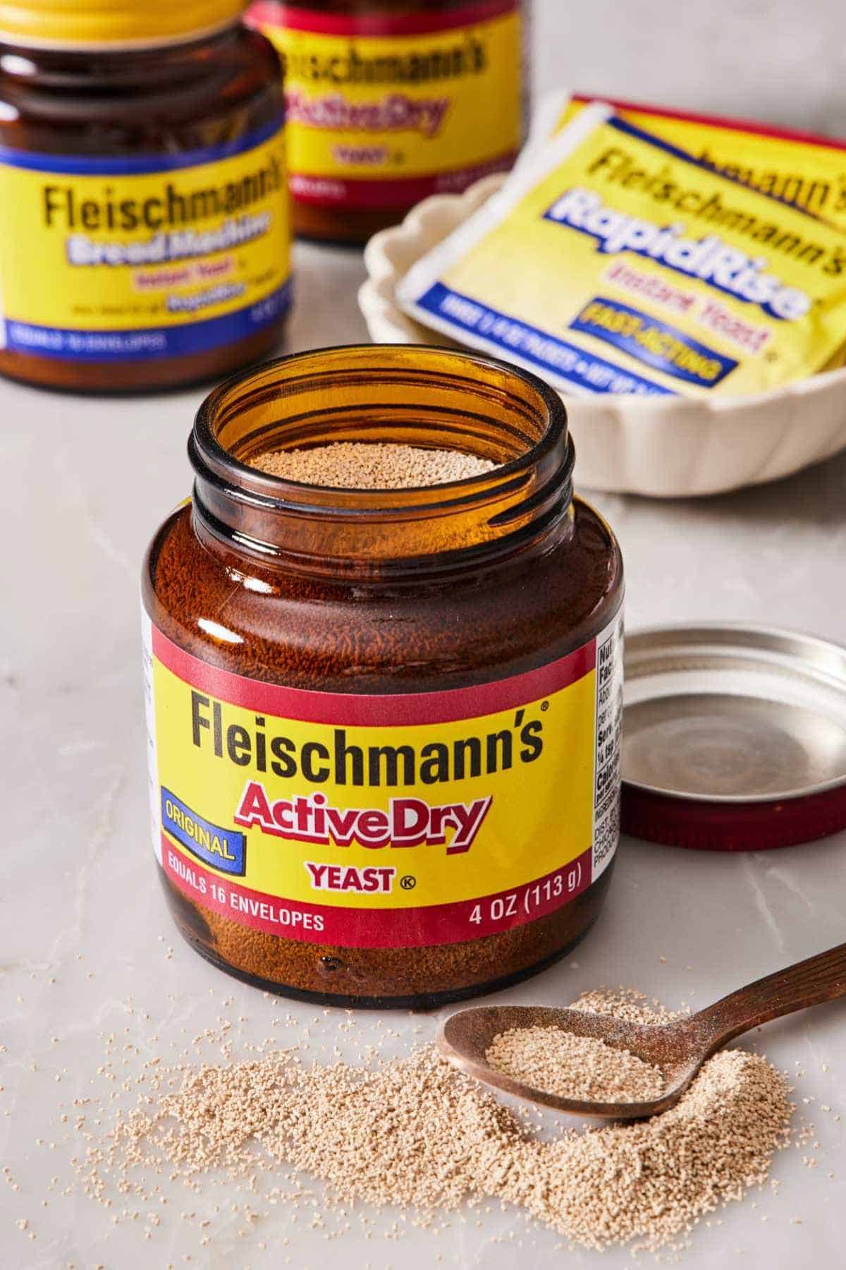 An open jar of active dry yeast with yeast sprinkled on the counter next to a spoon.