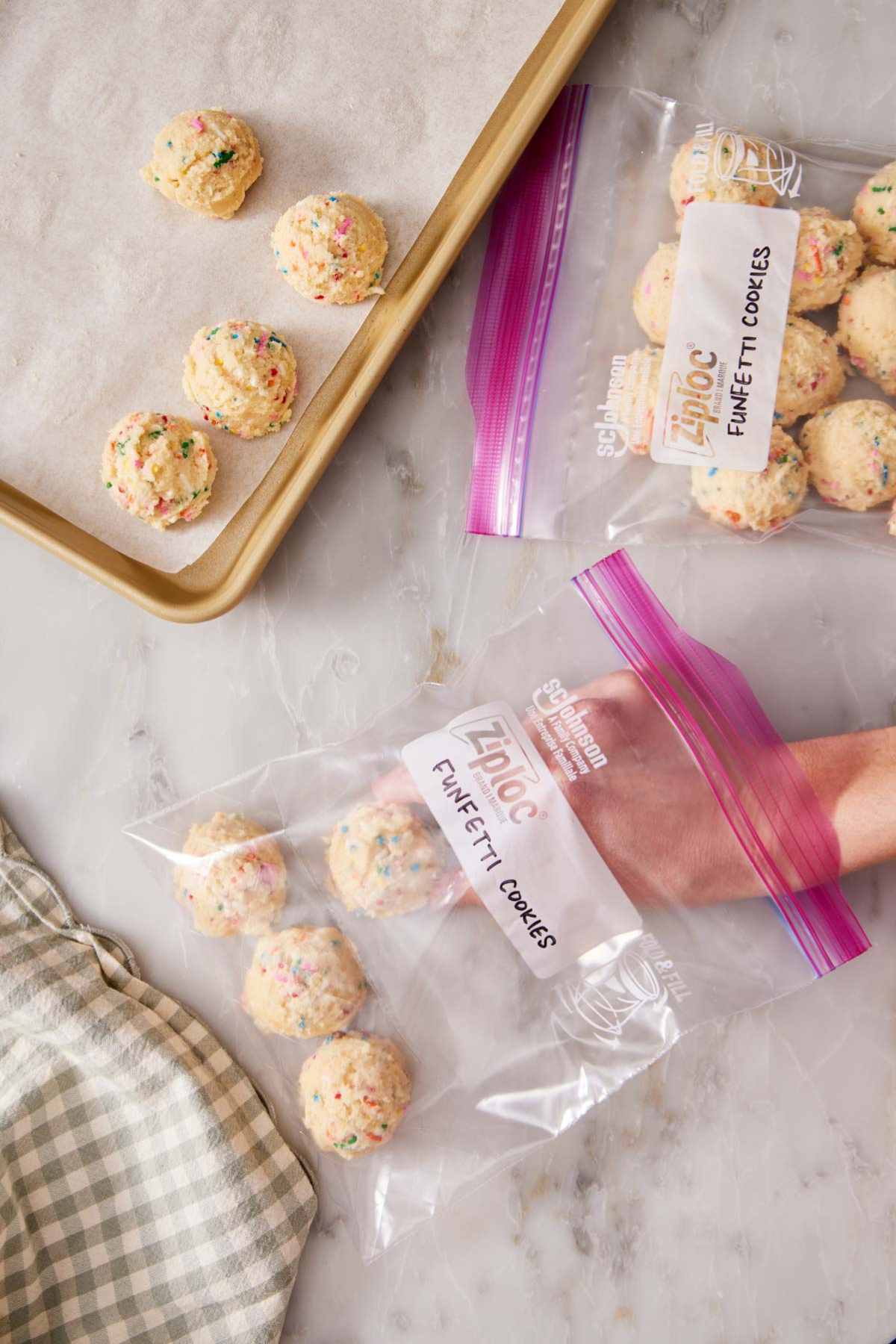 A few funfetti cookie dough balls on a baking sheet, and more in freezer bags.