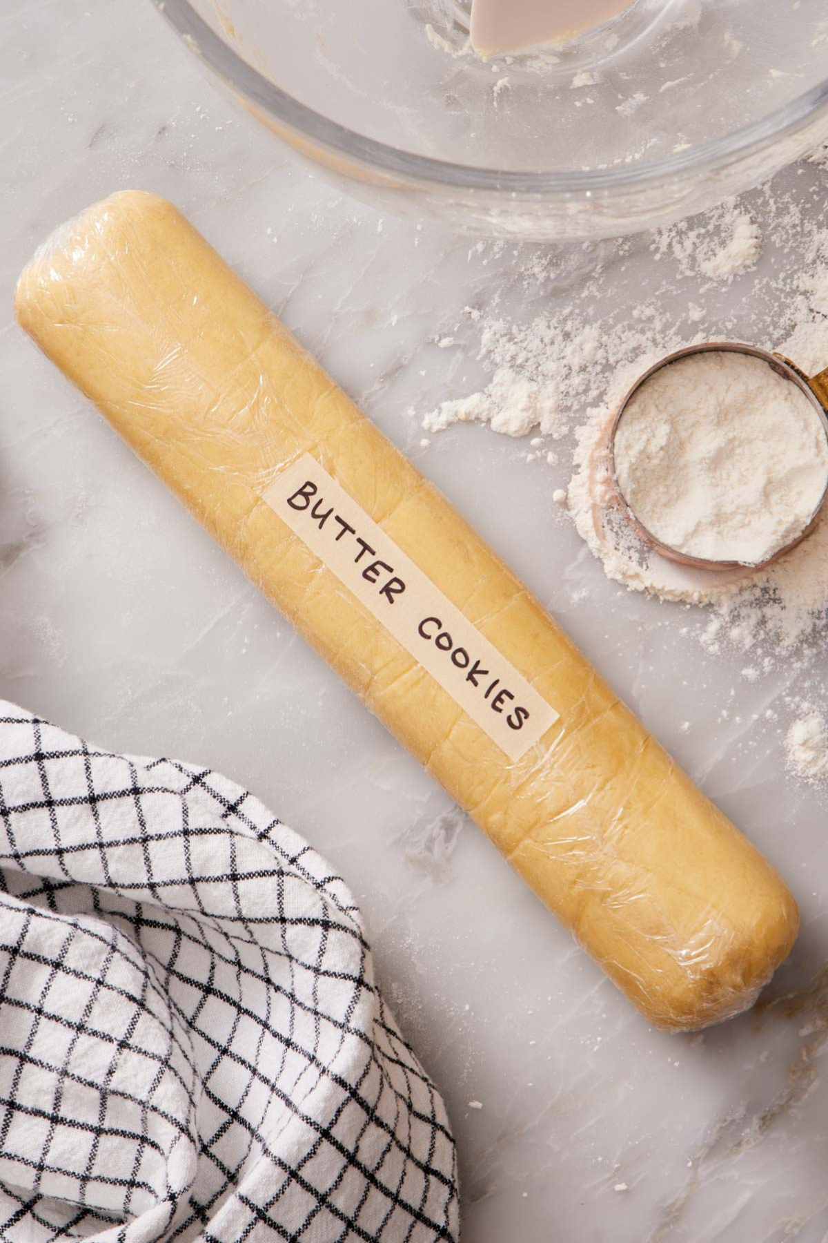 Slice-and-bake cookie dough log wrapped tightly with plastic wrap, with a measuring cup of flour alongside it.