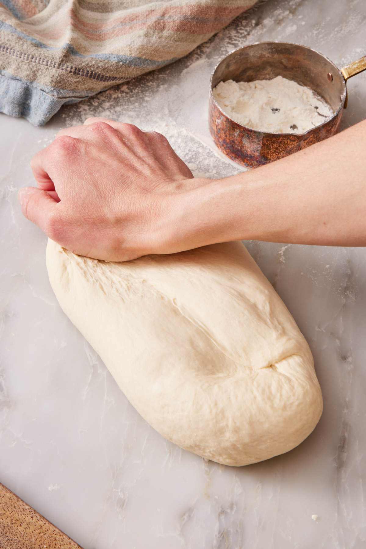 Hand kneading dough on a counter with a measuring cup with flour alongside.