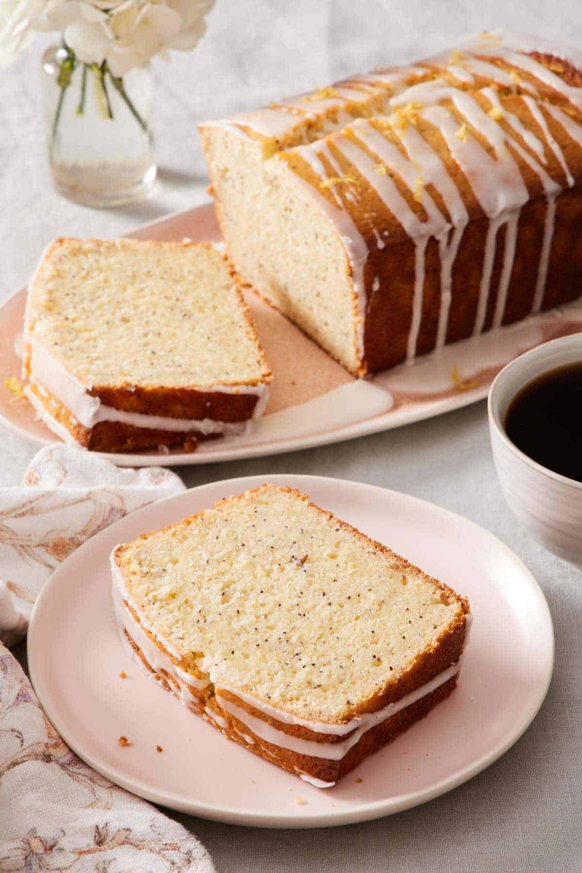A slice of lemon poppy seed loaf on a plate with the rest of the loaf in the background.
