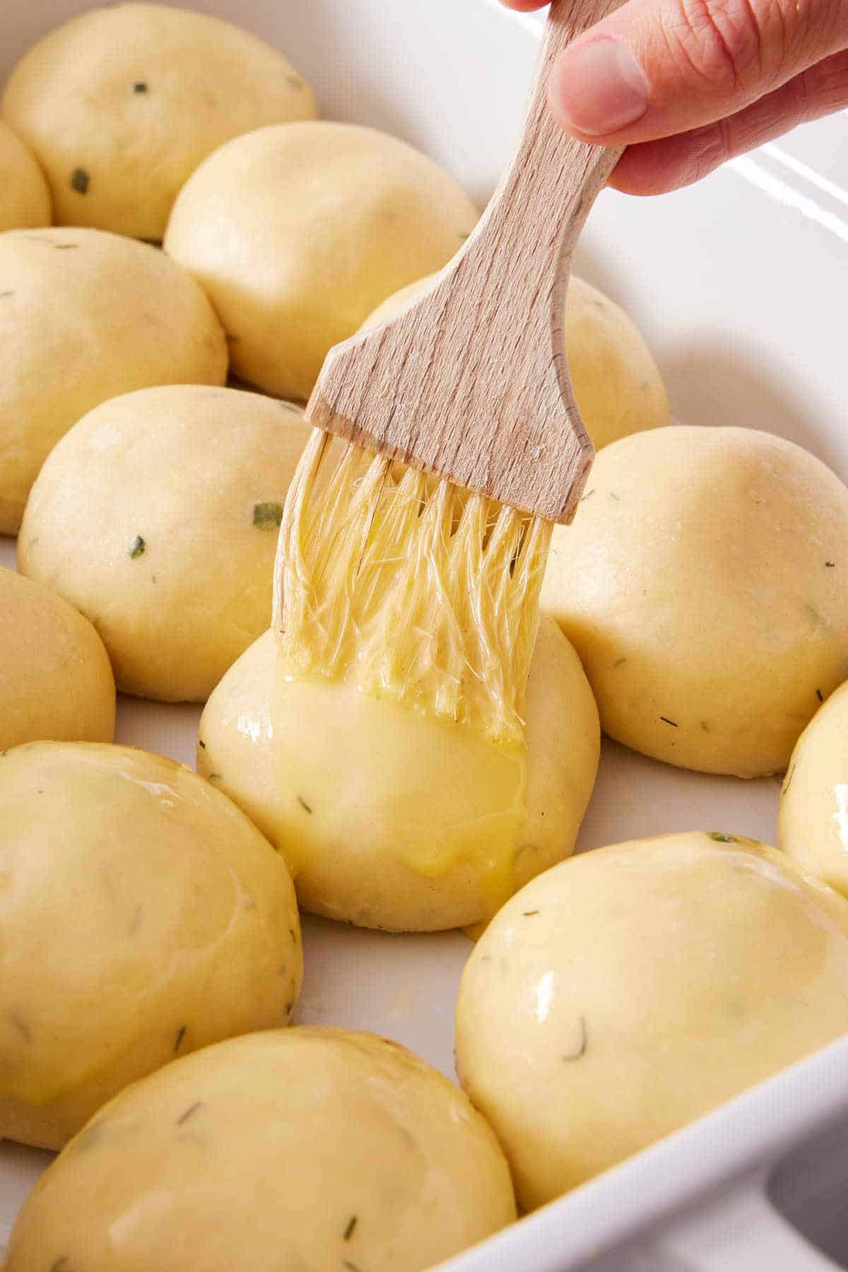 Close-up of melted butter brushed over rolled dough balls to make buns.
