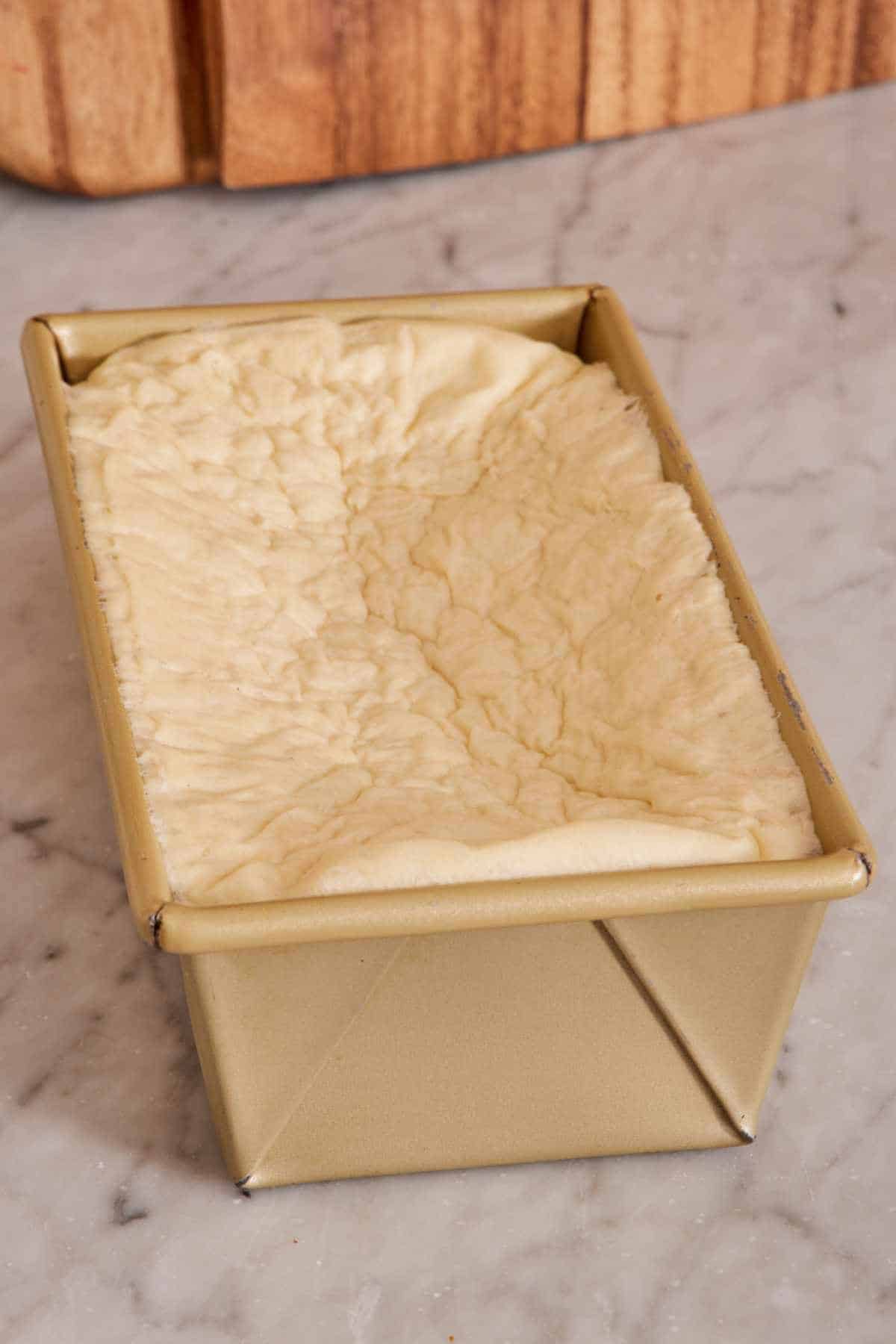 A loaf pan containing over-proofed dough, which has collapsed and is wrinkled.
