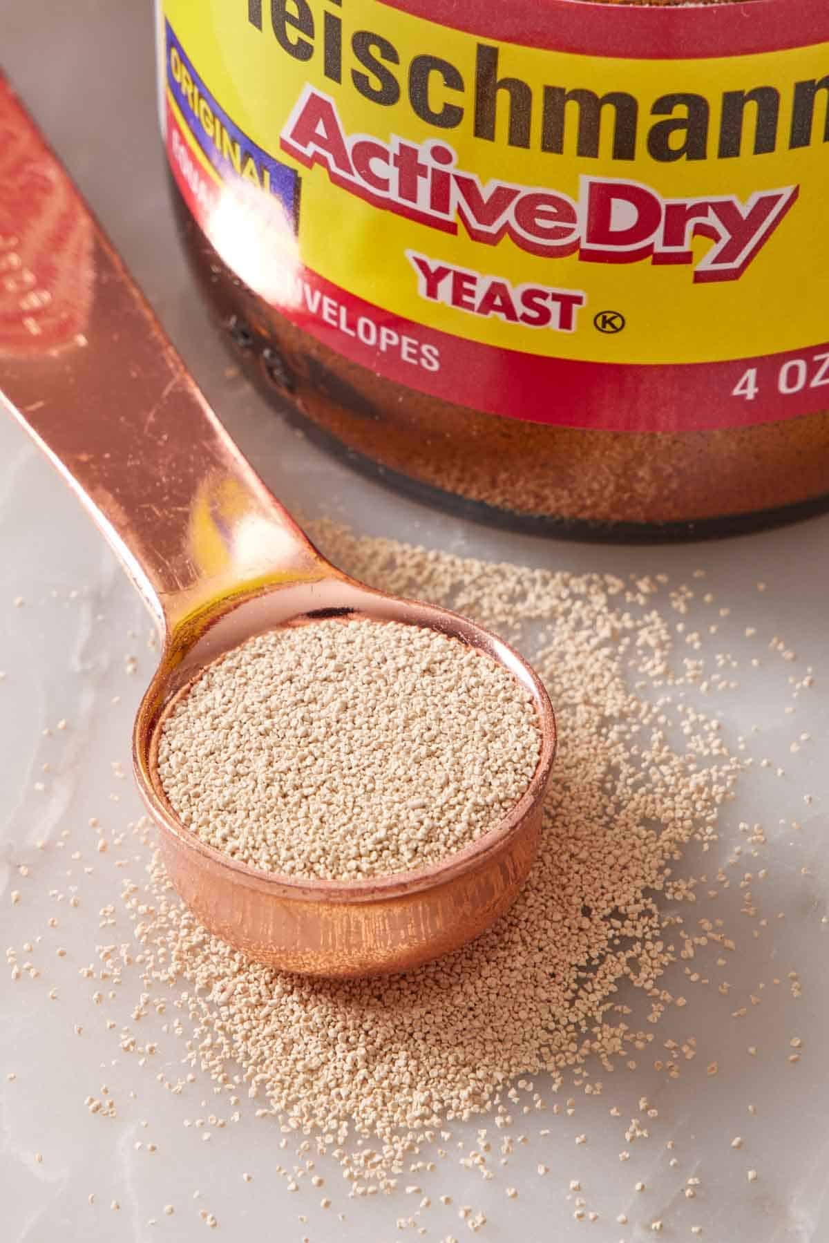 Close-up of active dry yeast in a measuring spoon with yeast sprinkled around it.