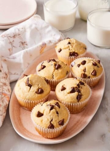 Chocolate chip muffins on a platter with glasses of milk in the background.