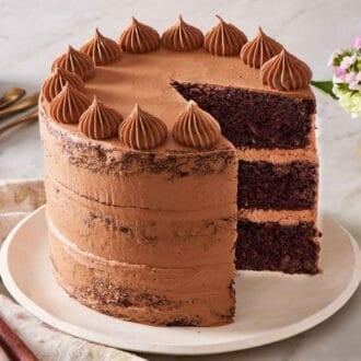 A chocolate zucchini cake with a slice removed with a small vase of flowers behind it.