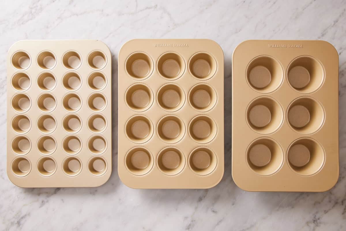 Three different cupcake pans in a row on a marble countertop.