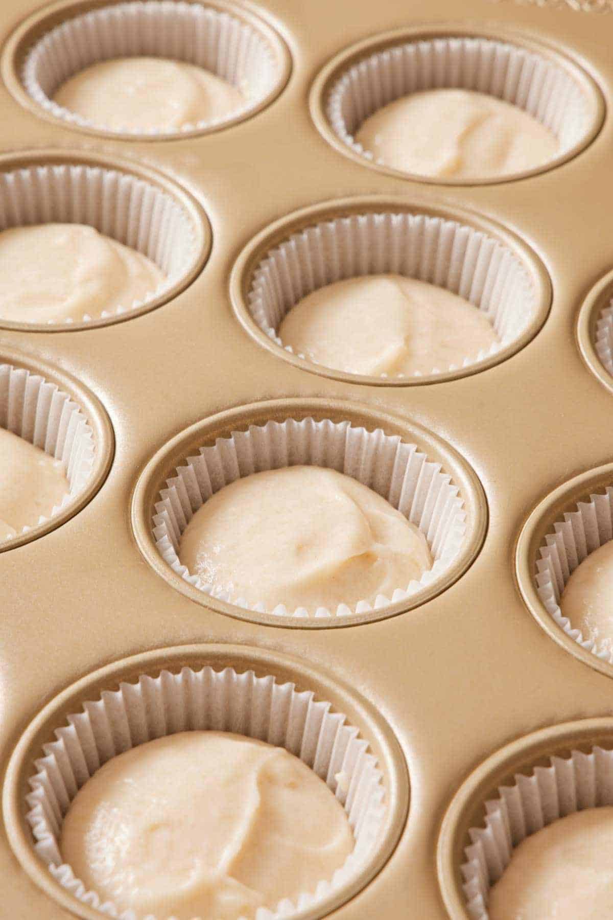 A muffin pan with paper liners and cupcake batter in the cavities.