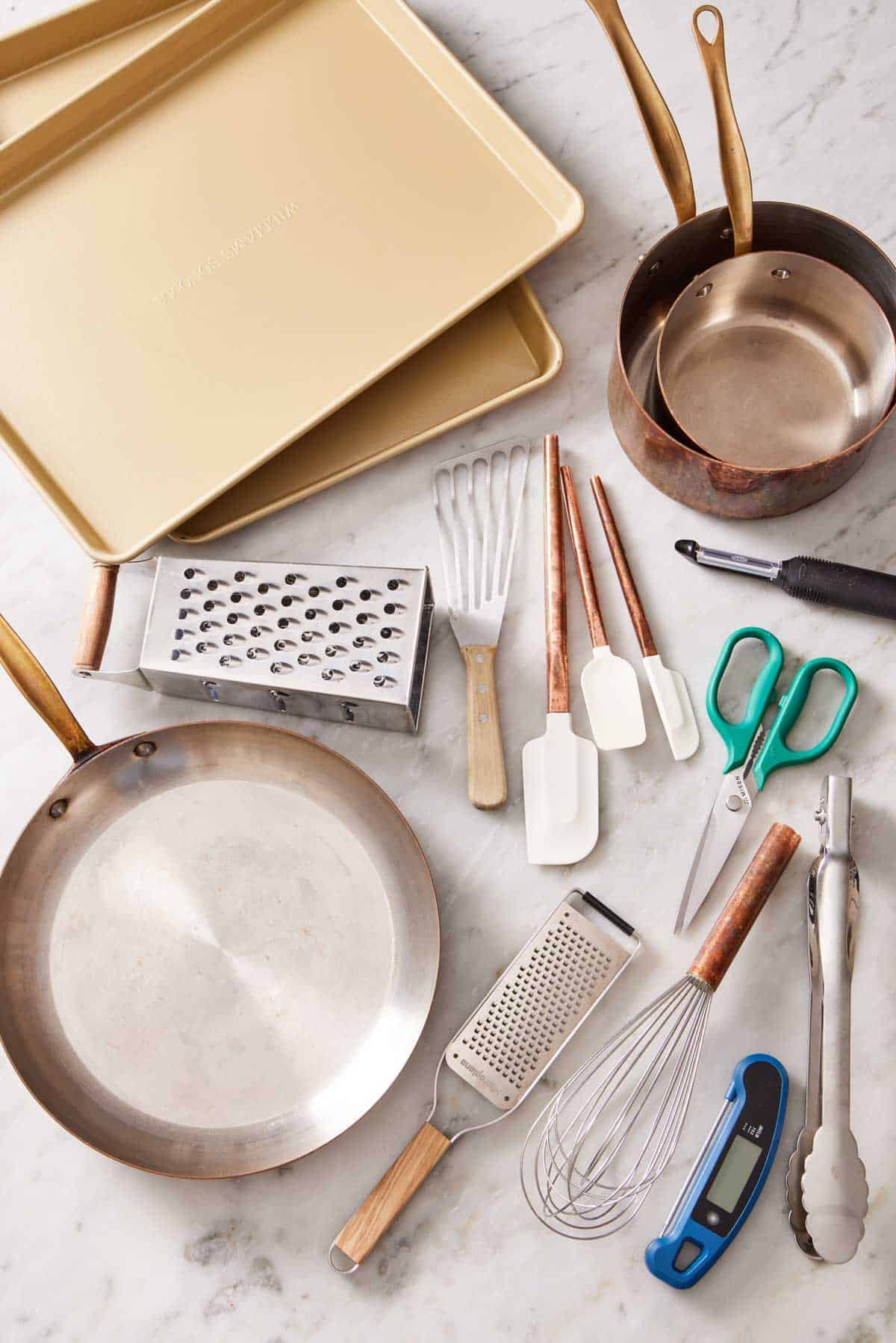 Overhead shot of various essential kitchen tools & essentials like pots, pans, spatulas, and baking trays.
