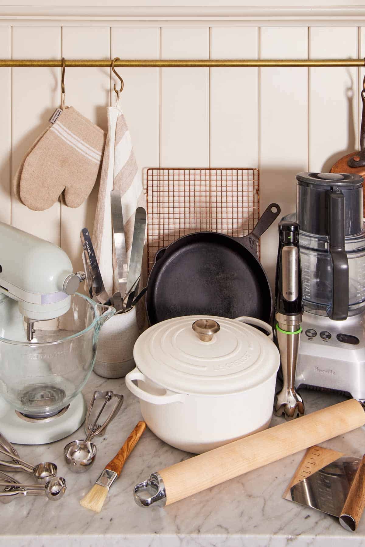 A stand mixer, immersion blender, Dutch oven, and more essential kitchen tools & essentials on a countertop.