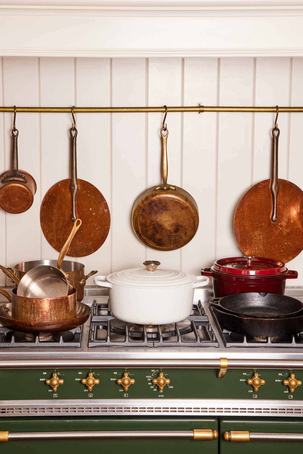 Pots and pans made of different materials set on a stovetop, with more pans hanging from hooks behind it.