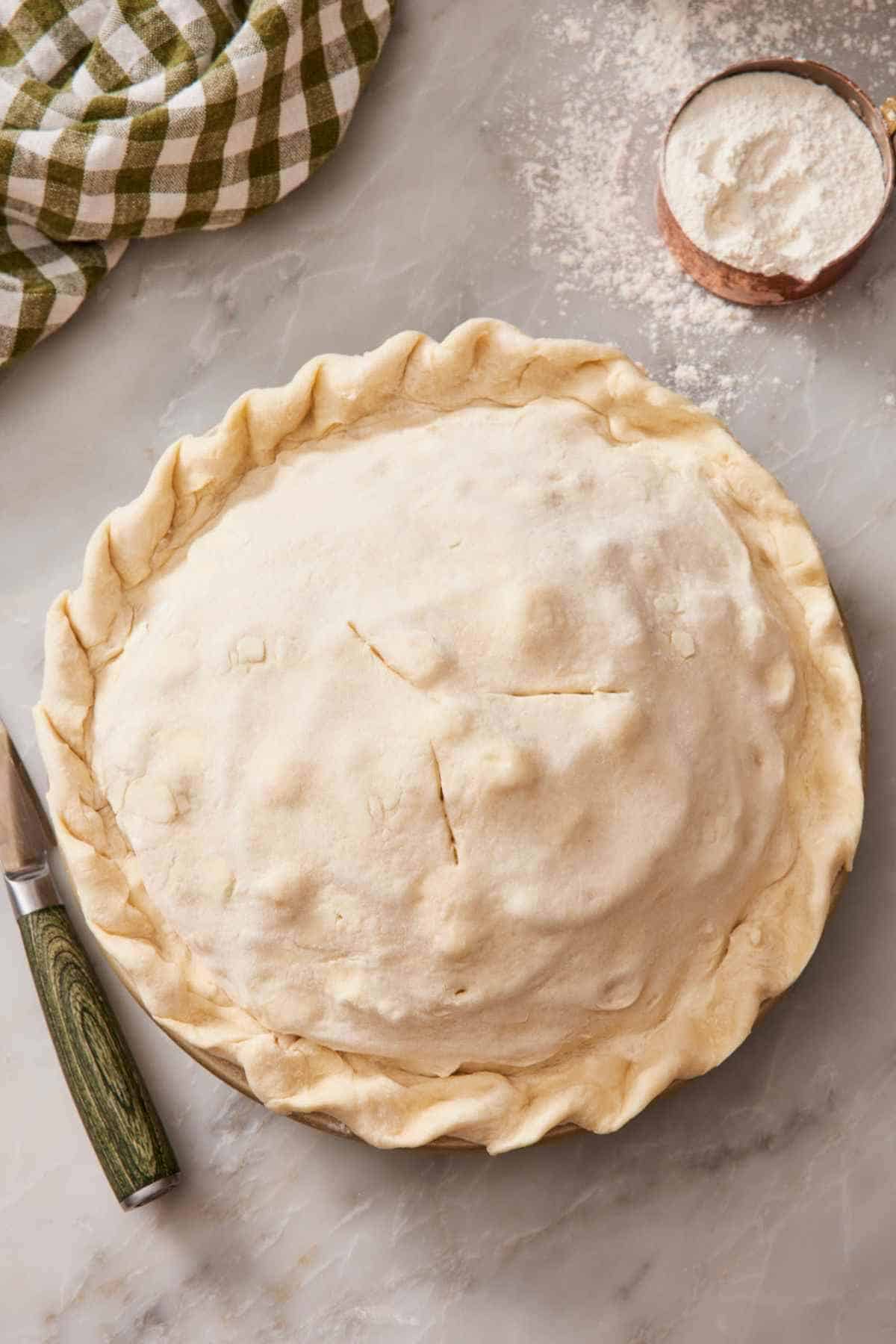 Overhead shot of a double crust pie on a counter with a cup of flour next to it.