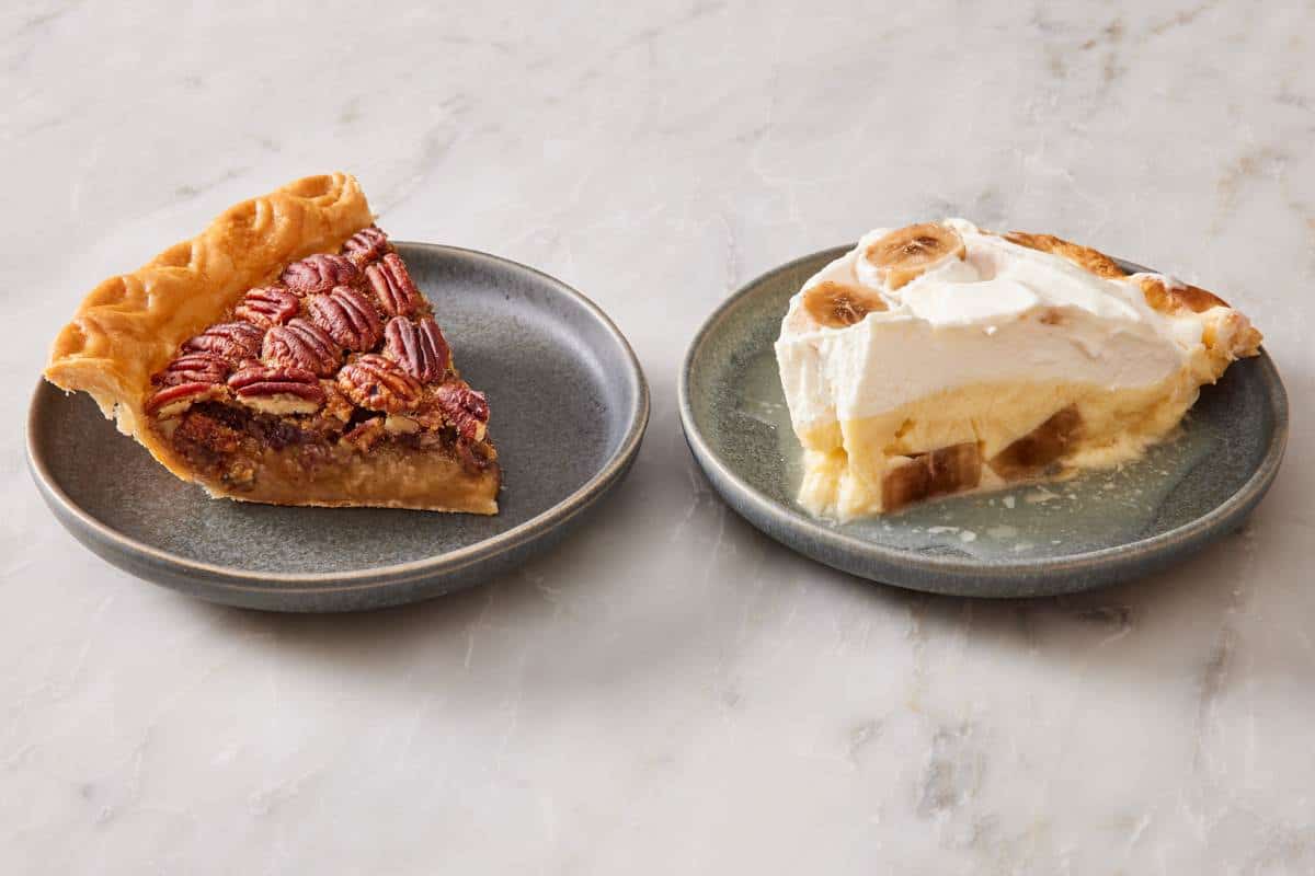 A slice of thawed pecan pie on a plate next to a slice of thawed banana cream pie on another plate.