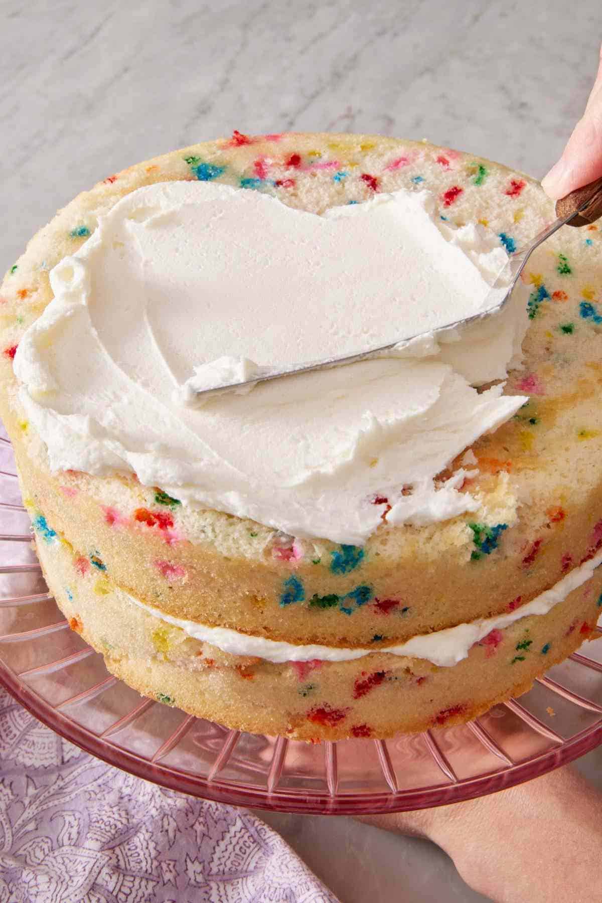 Frosting spread on top of a two-layer funfetti cake.