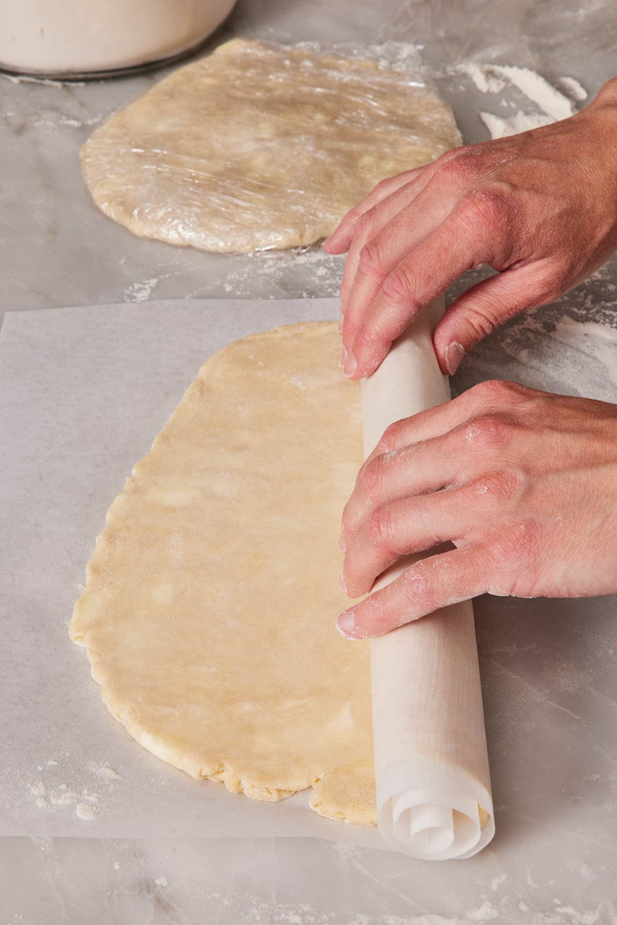 Rolled out pie crust dough rolled with parchment paper to prepare for freezing.