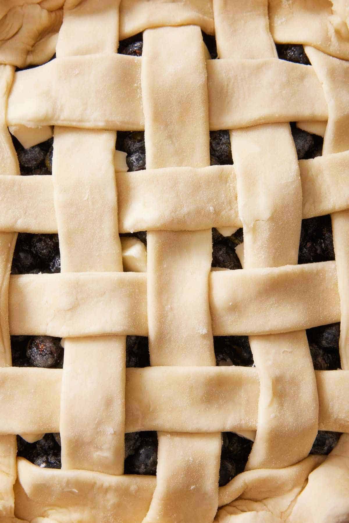 Close-up of an unbaked latticed pie crust showing blueberry pie filling underneath.