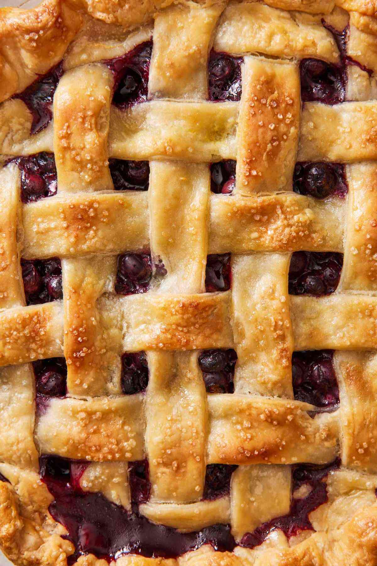 Close-up of a baked latticed pie crust showing blueberry pie filling underneath.