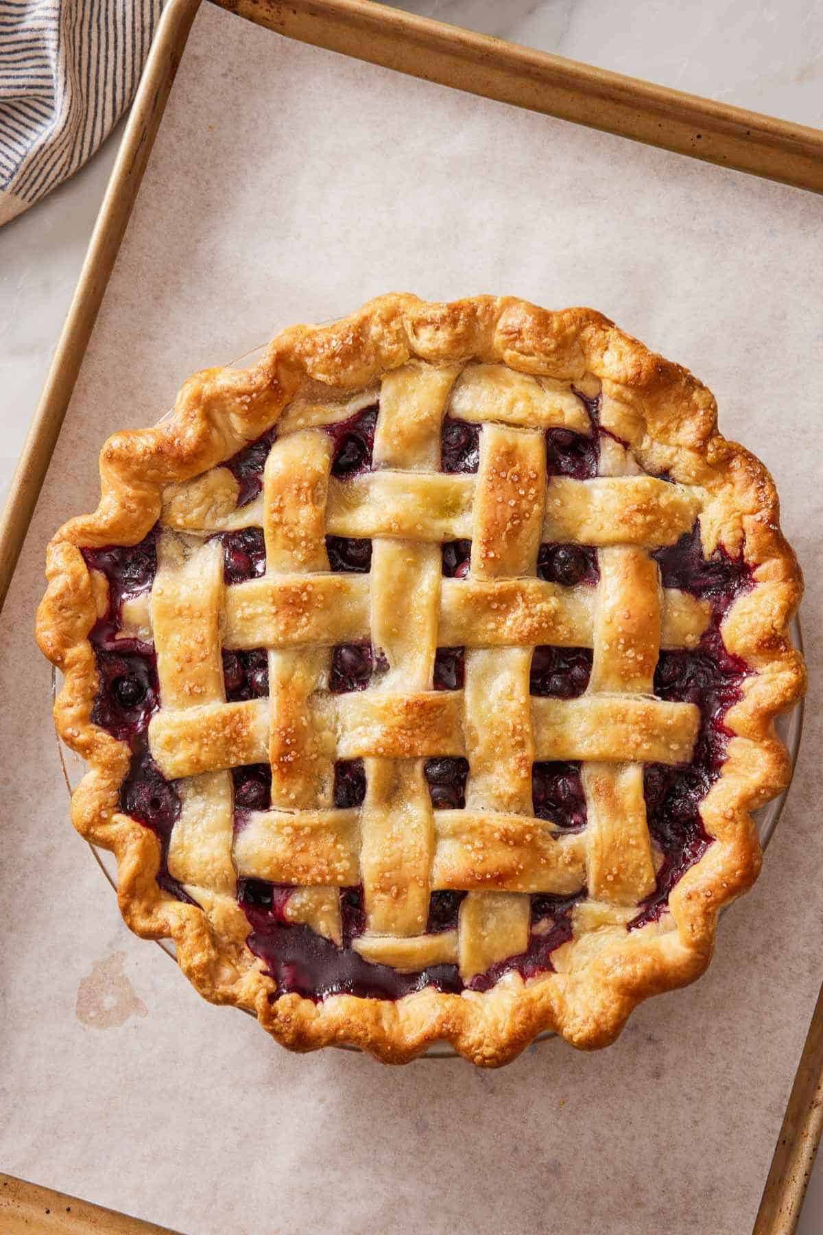 Overhead shot of a baked pie with a lattice top. The pie dish is set on a lined baking sheet.