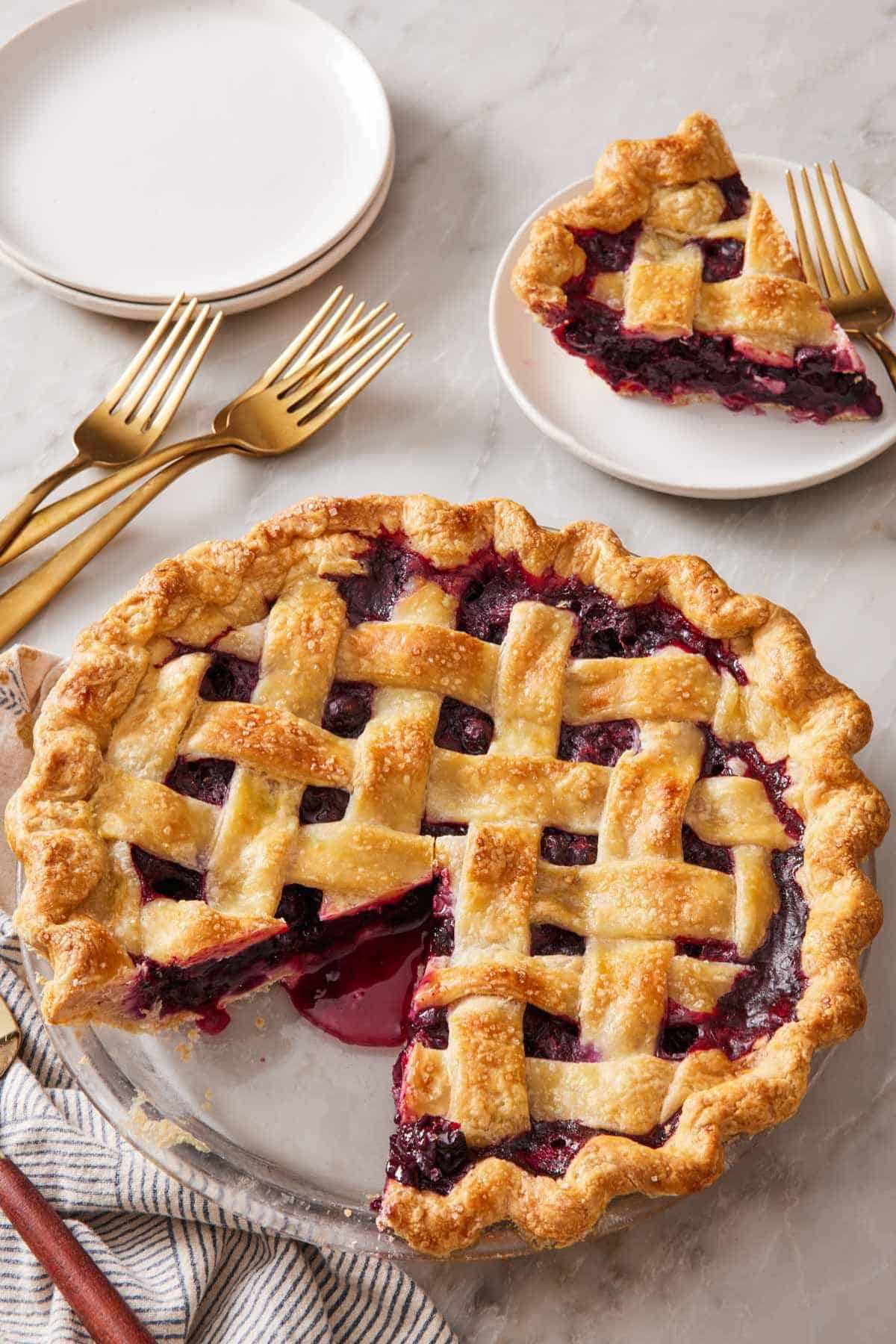 A pie with a lattice top with a slice cut out and served on a small plate in the background.