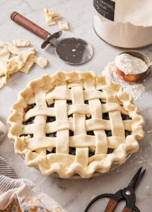 A pie with a lattice top on a counter with baking tools surrounding it.