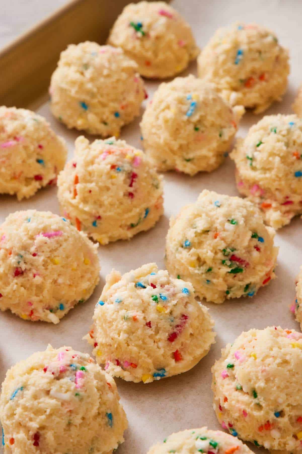 Funfetti cookie dough balls on a lined baking sheet.