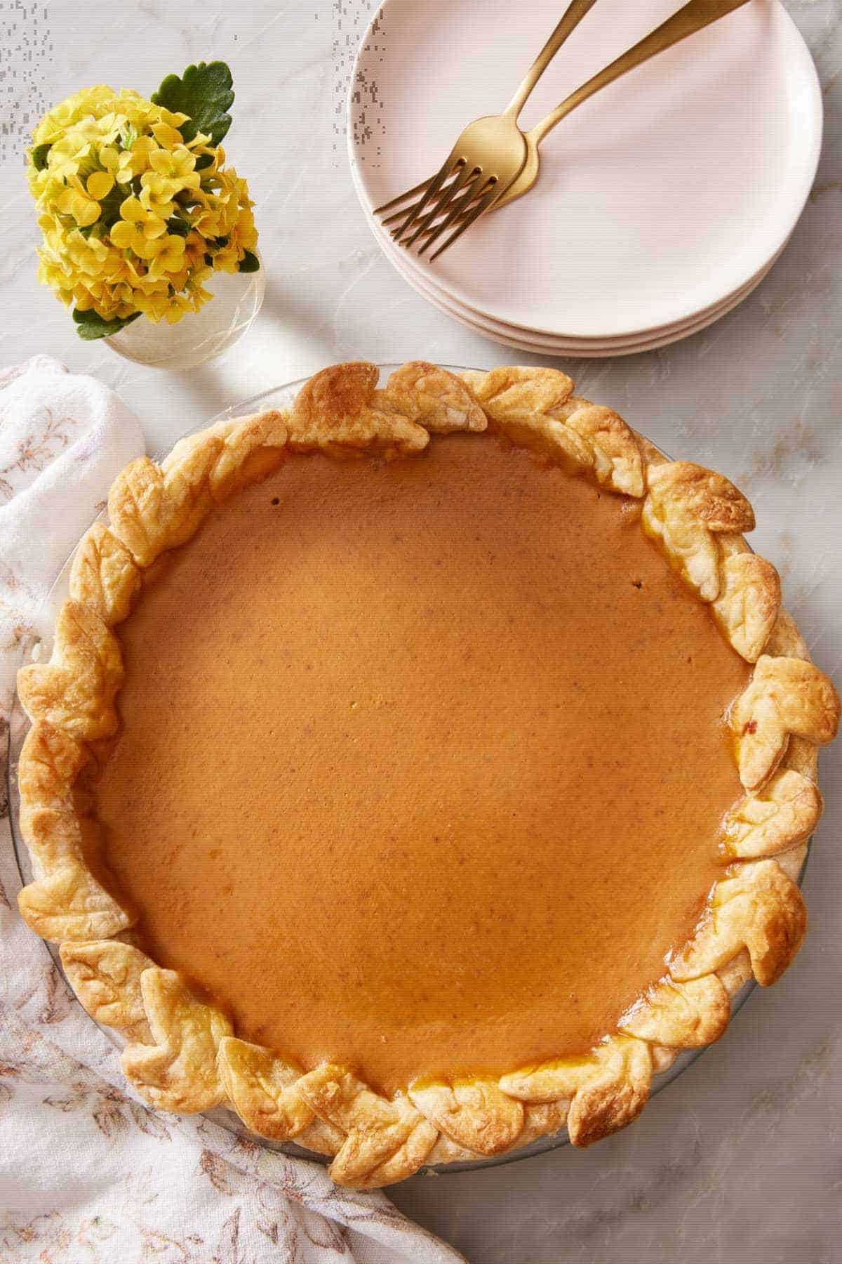 A baked pumpkin pie on a counter with small serving plates.