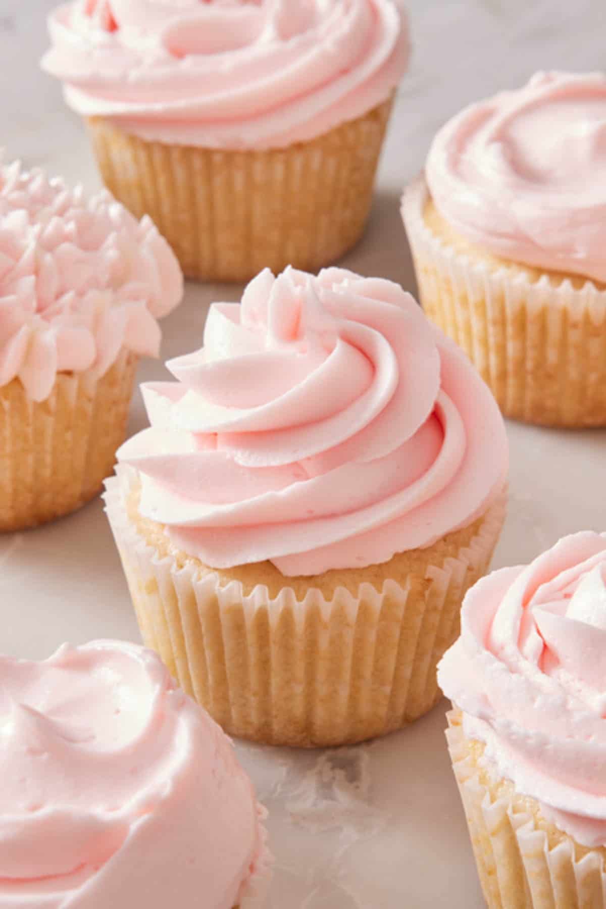 Cupcakes frosted with pink frosting on a marble countertop.
