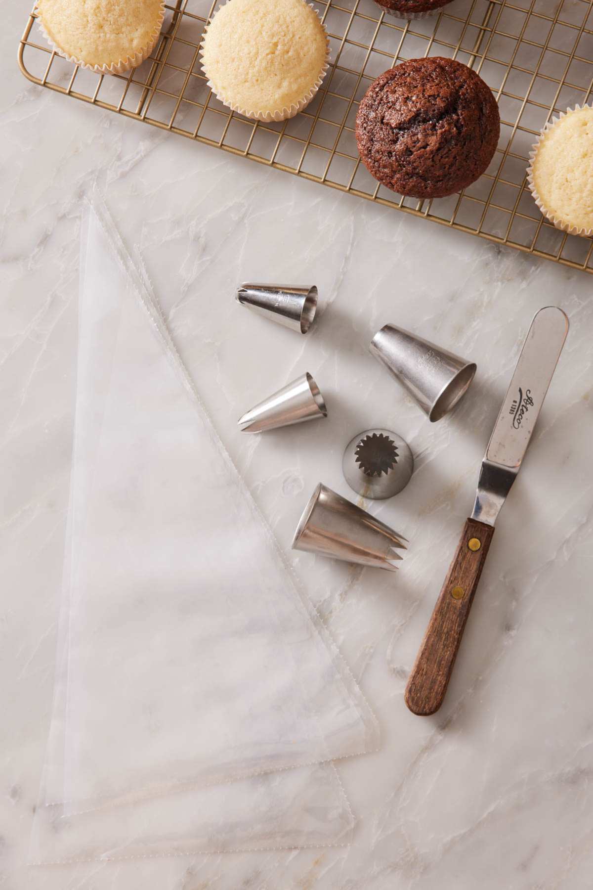 Equipment needed to frost cupcakes, with unfrosted cupcakes next to them.