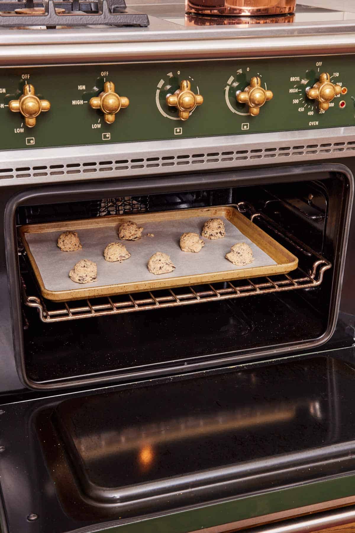 Cookie dough balls on a lined baking sheet in an oven.