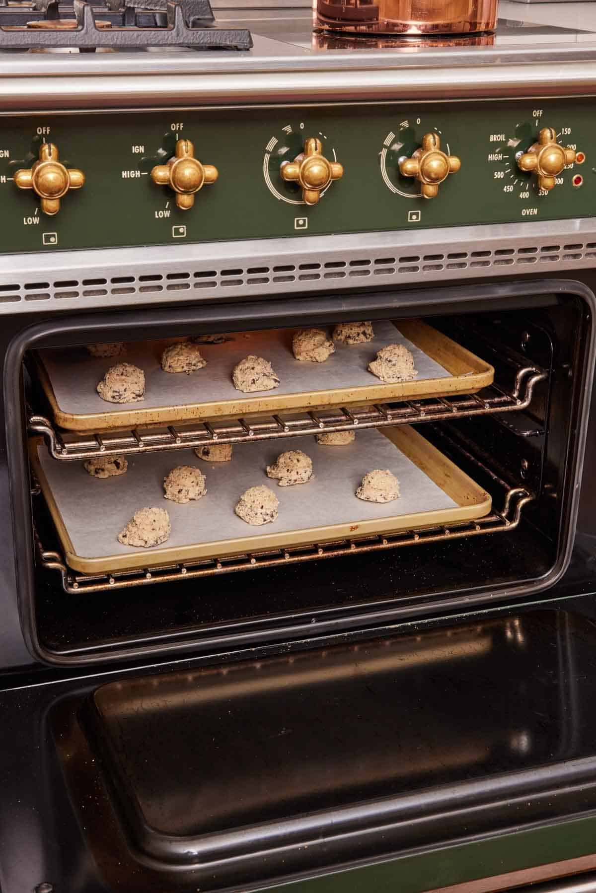 Two baking trays with cookie dough balls in an oven.