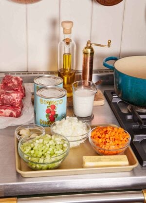 Mise en place with chopped vegetables, canned tomatoes, oil, and beef.