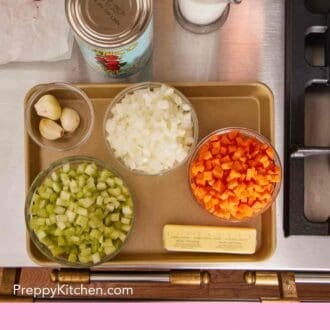 Pinterest graphic showing an overhead shot of various chopped veggies in a glass bowl, a stick of butter, canned tomatoes, and other ingredients.