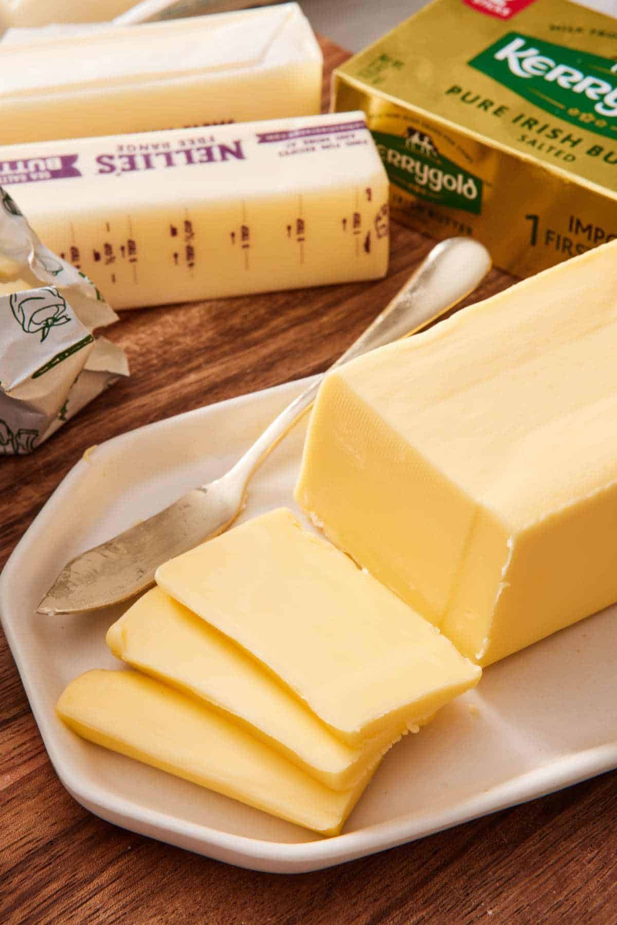 A block of butter on a platter with slices cut off. More butter in the background.