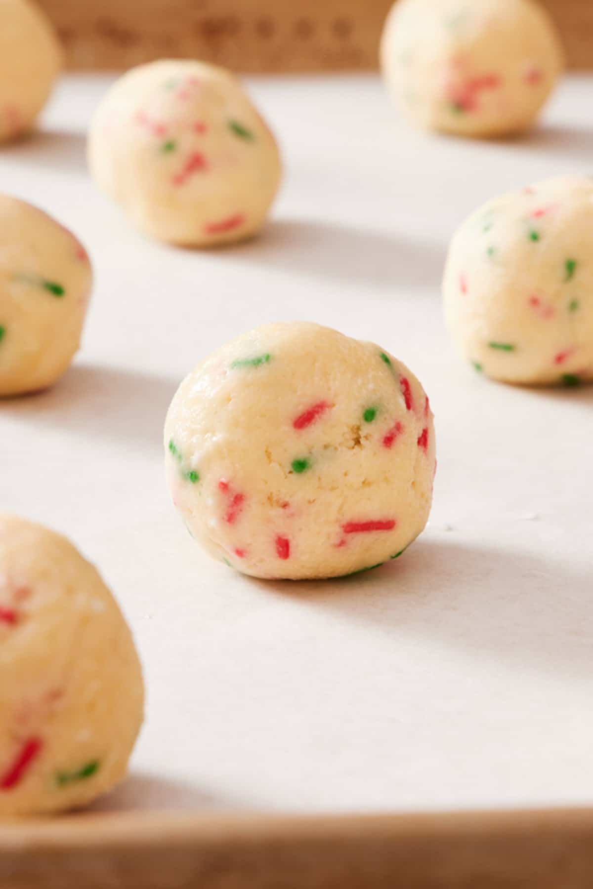Close-up of a funfetti cookie dough ball with more around it out of focus.
