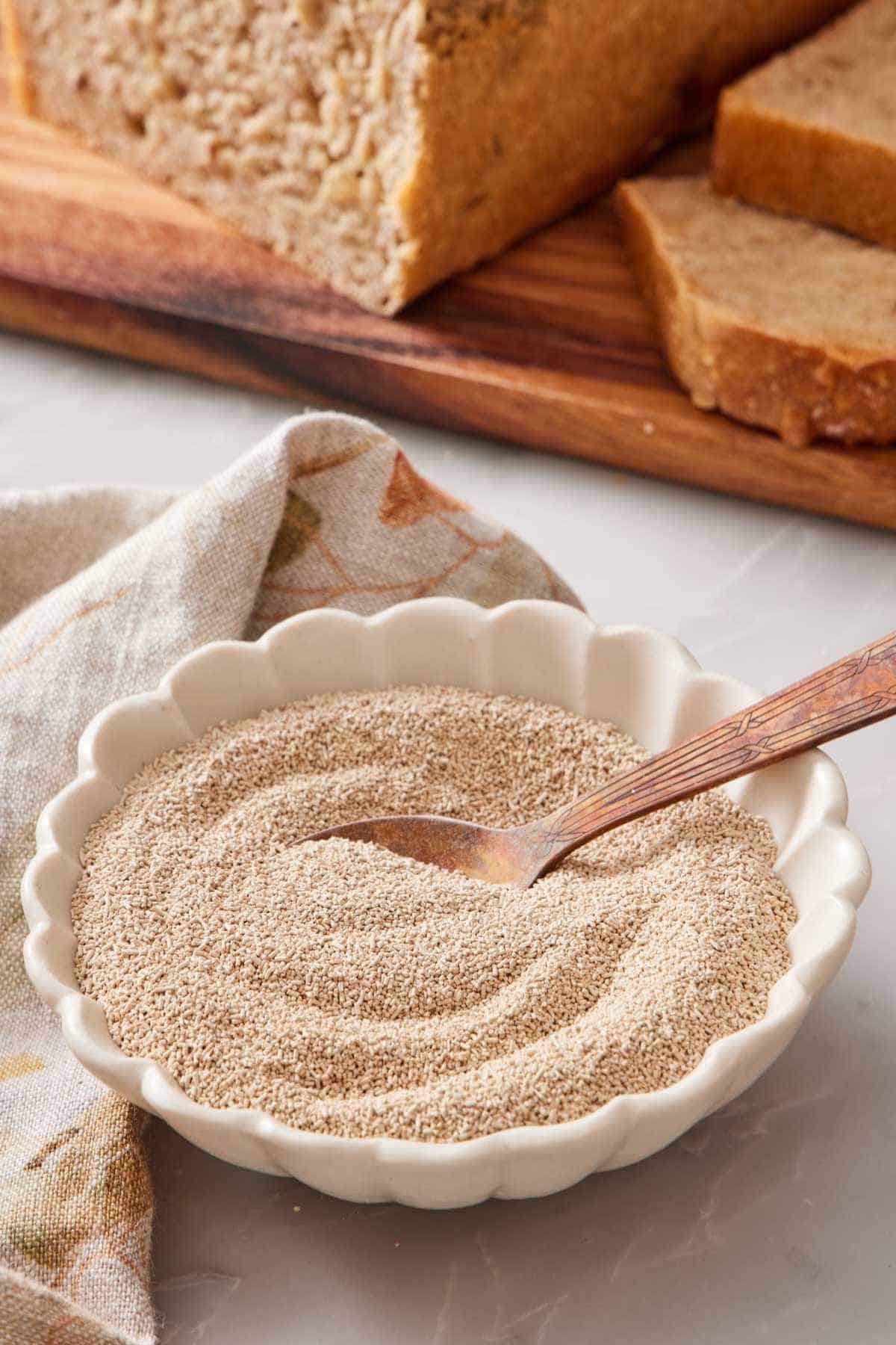 Dry yeast in a bowl with a spoon. A loaf of homemade bread out of focus in the background.