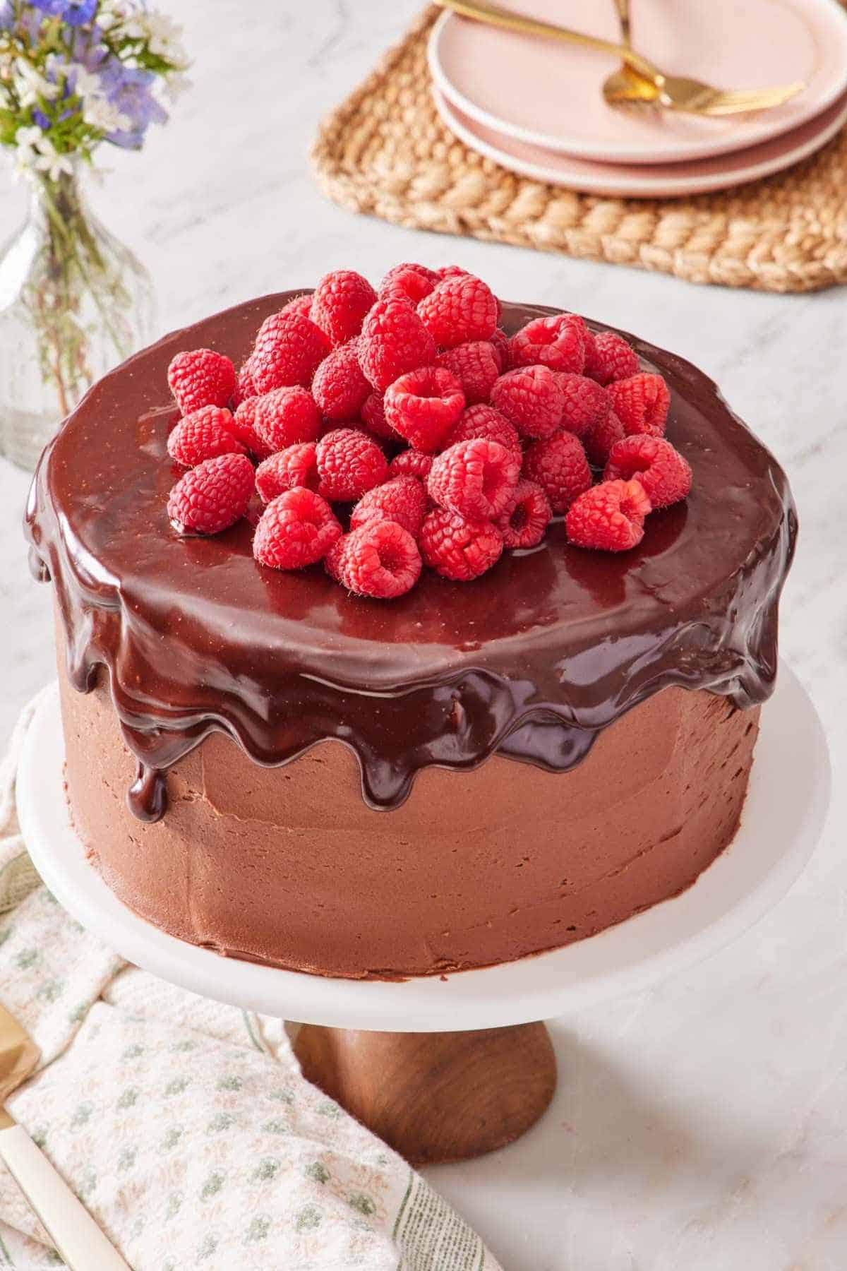 A homemade chocolate raspberry cake, on a cake stand, topped with fresh raspberries.