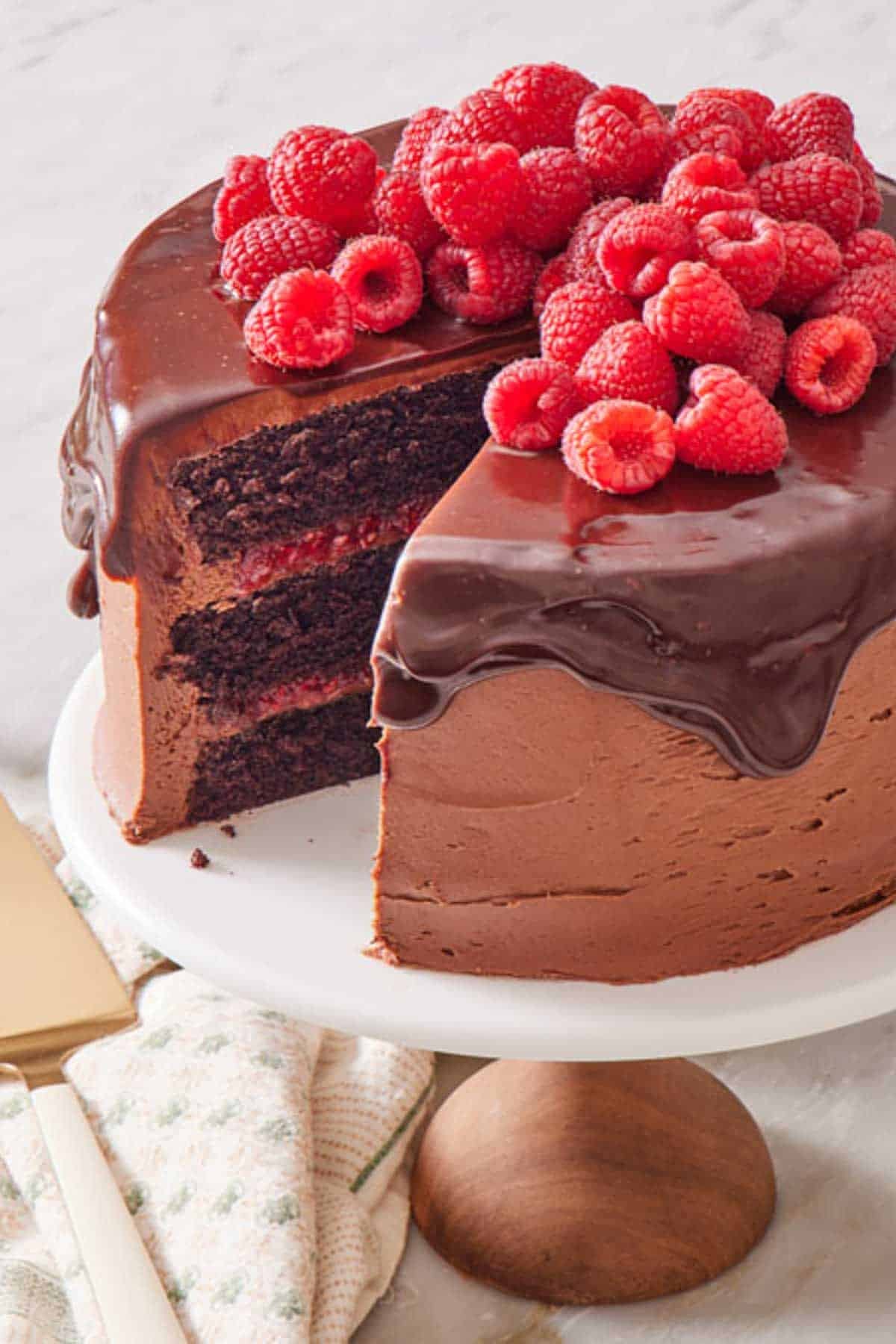 A chocolate raspberry cake on a cake stand with a slice cut out and removed.