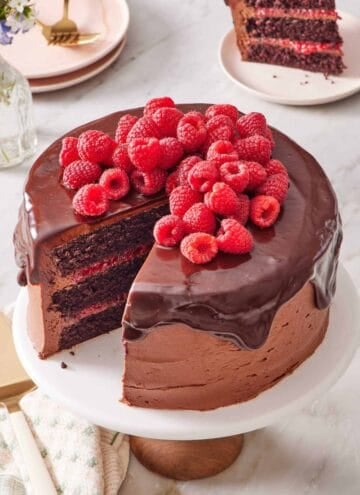 Chocolate raspberry cake on a cake stand with a slice cut out and placed on a plate behind it.