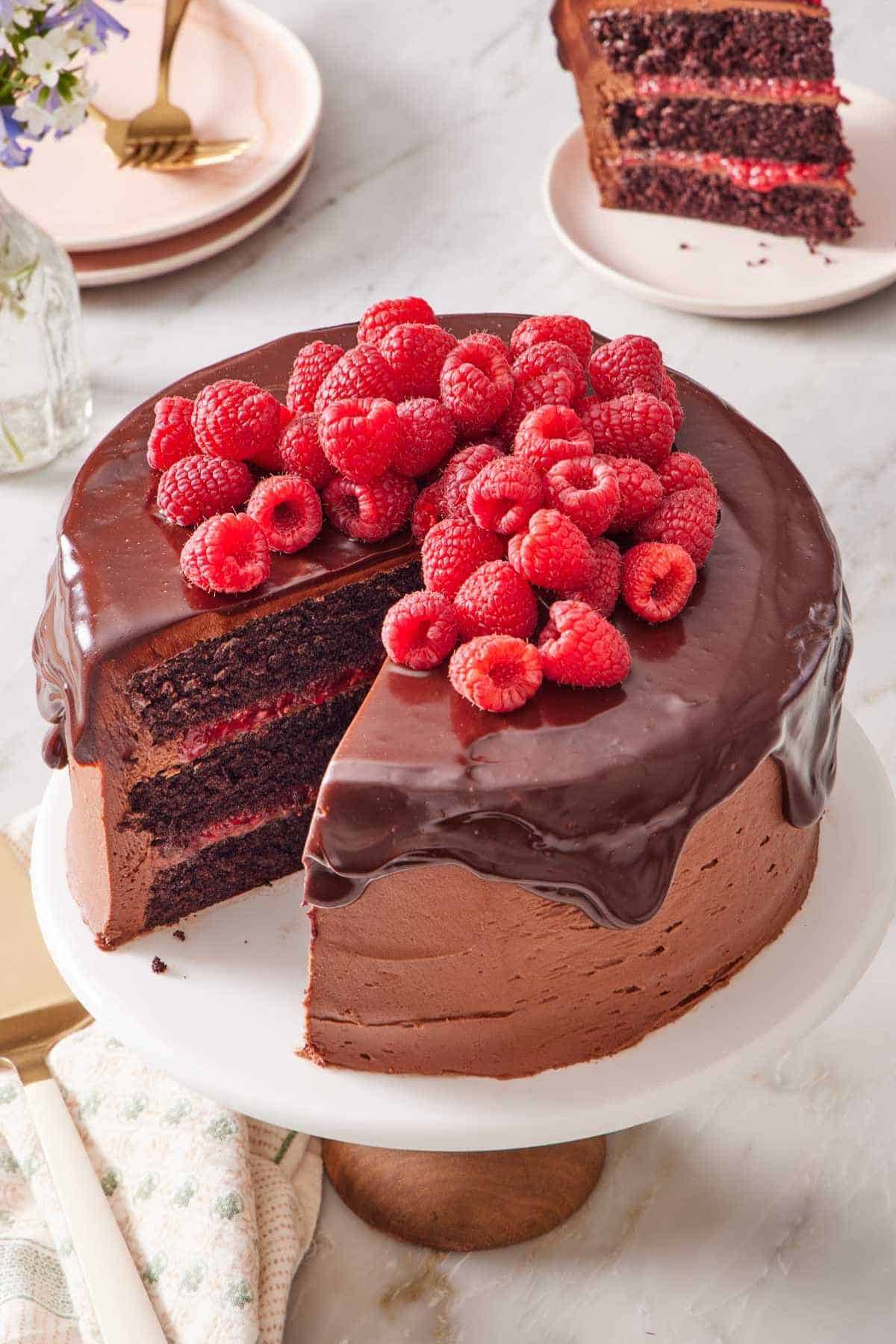 Chocolate raspberry cake on a cake stand with a slice cut out and placed on a plate behind it.