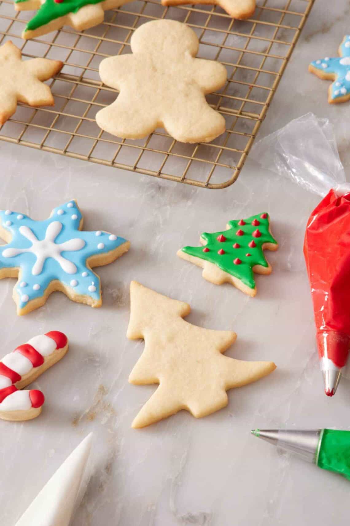 Some decorated and some plain cookies on a countertop and on a wire rack.