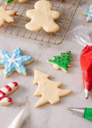 Some decorated and some plain cookies on a countertop and on a wire rack.