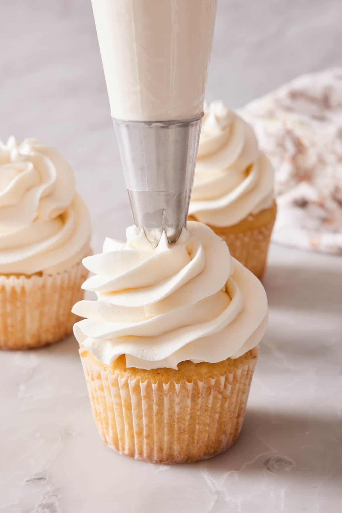A vanilla cupcake frosted with buttercream with a piping tip.