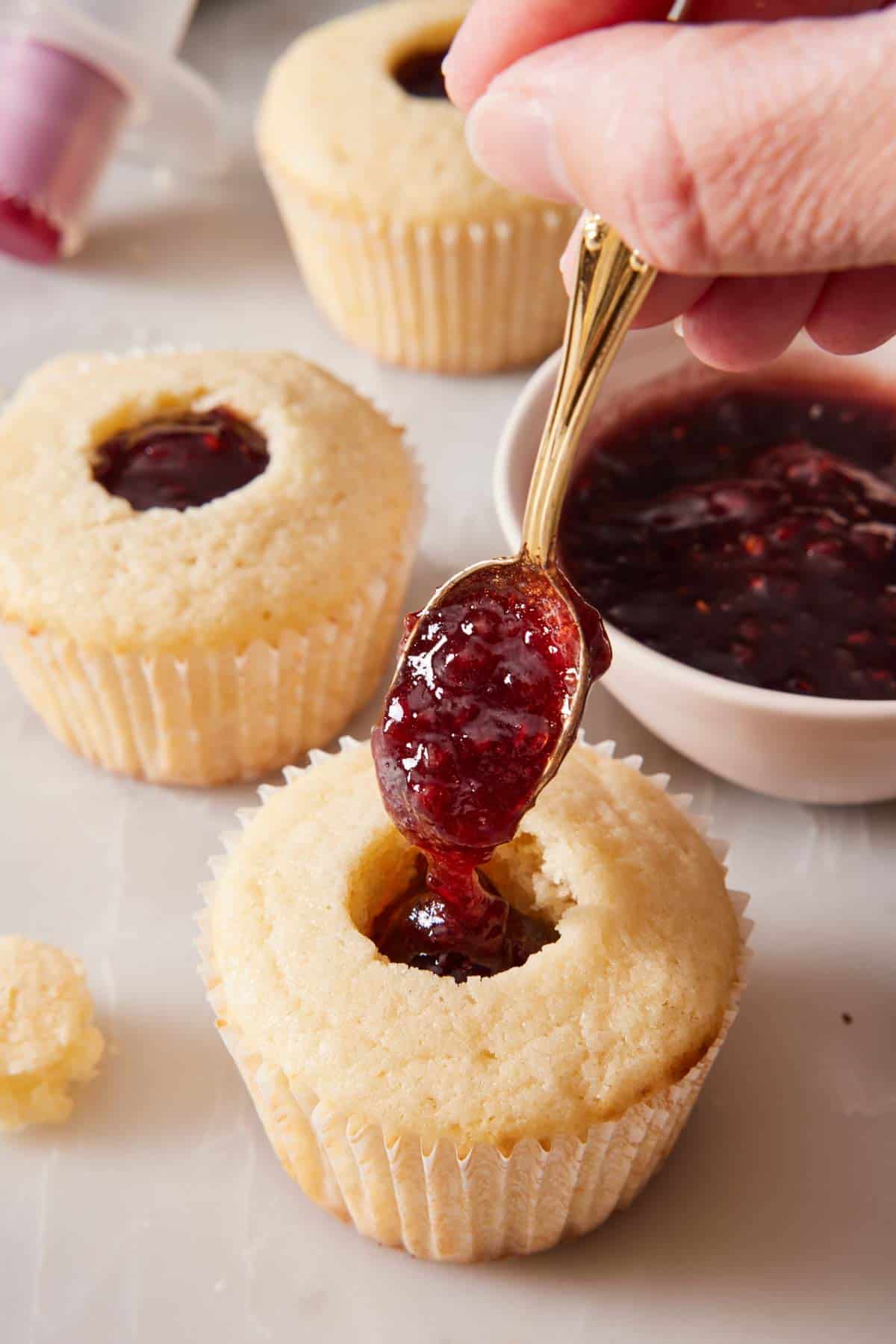 Cupcakes being filled with fruit jam on a marble countertop.