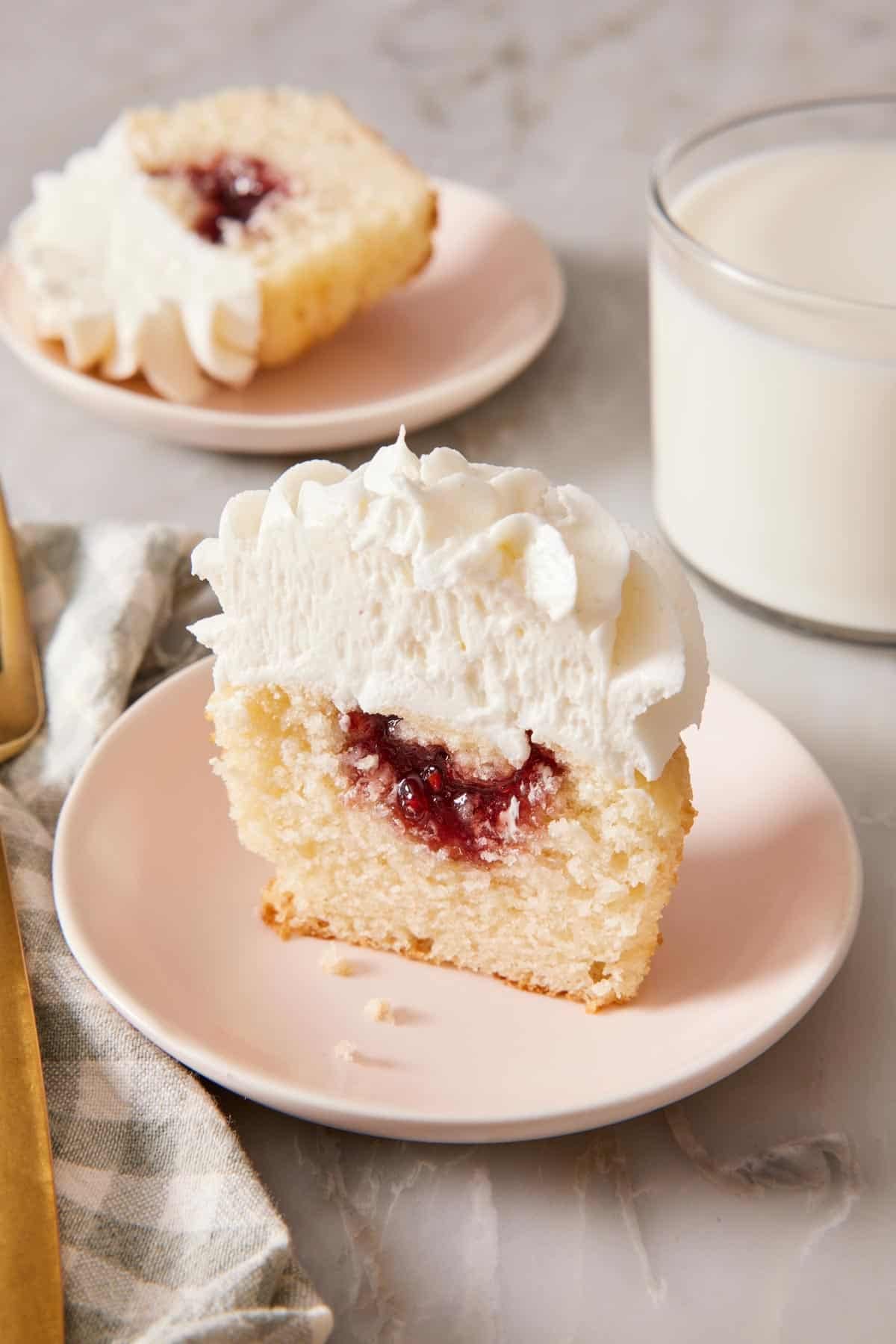 Close-up of a halved cupcake on a plate showing the filling. A glass of milk and the other half of the cupcake just behind.
