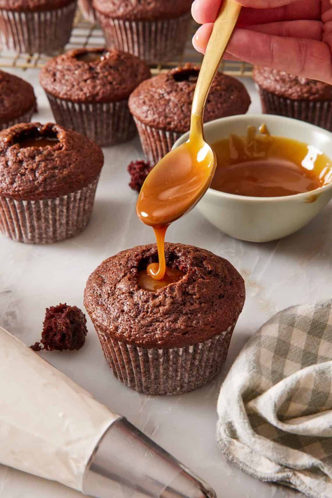 A chocolate cupcake being filled with caramel sauce, with more filled cupcakes in the background.
